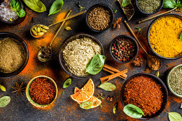 Set of Spices and herbs for cooking. Small bowls with colorful  seasonings and spices - basil, pepper, saffron, salt, paprika, turmeric. On black stone table top view copy space