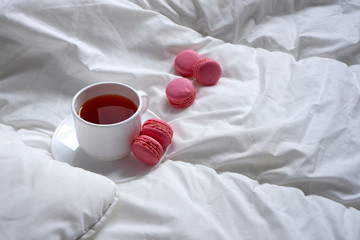 A Cup of tea with a saucer on a white soft blanket and macaroons .  Soft white bed linen. Background.  Minimalism.