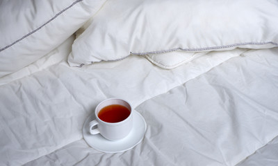 Fototapeta na wymiar A Cup of tea with a saucer on a white soft blanket. Soft white bed linen. Background. Minimalism.