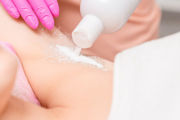 Close up of cosmetologists hand sprinkling talcum powder on a armpit of young woman before the depilation procedure.