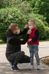 Fototapeta premium Little blonde girl with her father in medical masks in the park