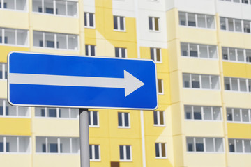 Road sign traffic to the right on the background of a new multi-storey building not yet populated. Housewarming, sale of new apartments and studios