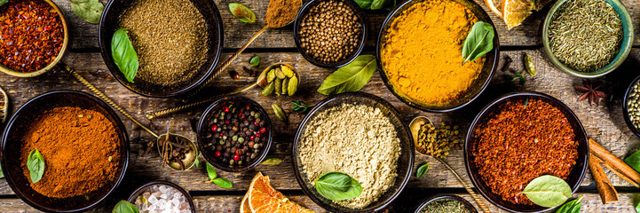 Set of Spices and herbs for cooking. Small bowls with colorful  seasonings and spices - basil, pepper, saffron, salt, paprika, turmeric. On rustic wooden plank table background, top view copy space