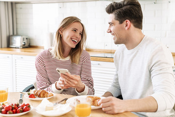 Obraz na płótnie Canvas Portrait of young happy couple using smartphone while having breakfast