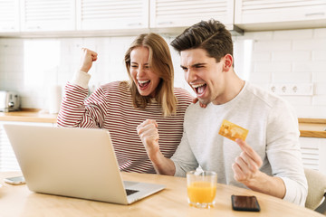 Portrait of couple using laptop and card while making winner gesture
