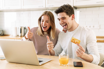 Portrait of couple using laptop and credit card while showing thumbs up