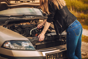 Worried young woman with her broken car with a wrench in her hand