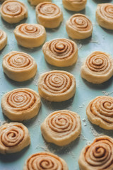 Homemade sweet pastry cinnamon rolls buns dough, white flour on the blue background. Semi-cooked. Pattern