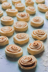 Homemade sweet pastry cinnamon rolls buns dough, white flour on the blue background. Semi-cooked. Pattern