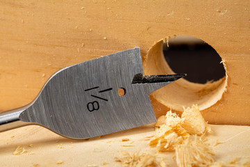 closeup of a wood boring spade bit drilling a hole in a piece of wood