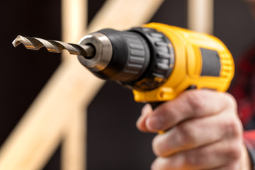 close up of a worker holding an electric drill with a high speed metal drill bit pointing at the...