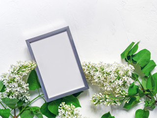 Spring or summer flower arrangement. An empty metal photo frame and a white blooming lilac are on a white textured background.Top view. Flat lay. Copy space.