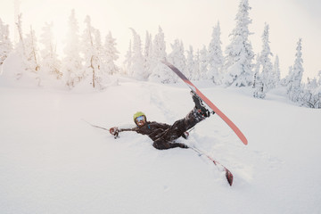 Male skier falling down on fresh snow powder between snow-covered trees. Sunny winter day and free...