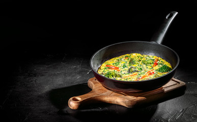 Tasty frittata with spinach and herbs in an iron frying pan on an dark background. Fritatta with broccoli