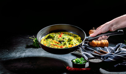 Tasty frittata with spinach and herbs in an iron frying pan on an dark background. Fritatta with broccoli