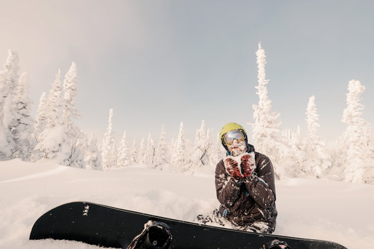 Male snowboarder relaxing and enjoy sunny winter day on snow powder in snow-covered spruce trees