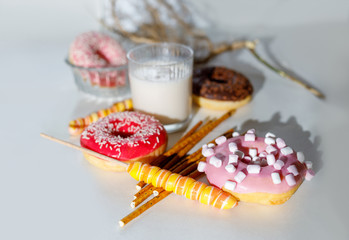 colored donuts on a light background, a glass of milk, candy on a stick and straws