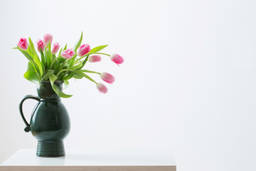 pink tulips on green jug on white background