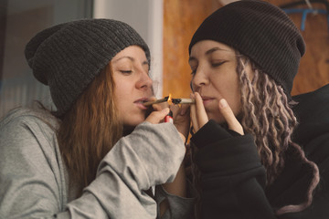 Female friends wearing hats and rasta dreadlocks hair style smoking self-roll weed cigarette