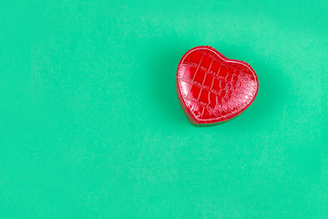 Close-up of a red leather jewelry box in the shape of a heart, on a green background. The view from the top. Concept of gifts and love