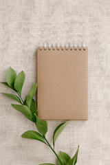 Blank brown vintage notebook, leaves, on beige linen fabric. Minimalistic workplace concept. Top view on background with copy space. Summer flat lay
