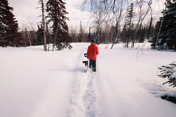 Male snowboarder holding board walking in deep snow in forest