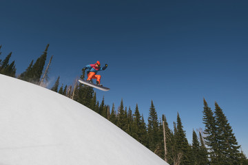 snowboarder male jumping above snowy ski slop. Sunny day in ski resort, beautiful mountains...