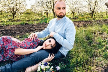 Naklejka na ściany i meble Lovestory in a blooming apple garden. Loving couple lying on the grass tenderly hugging