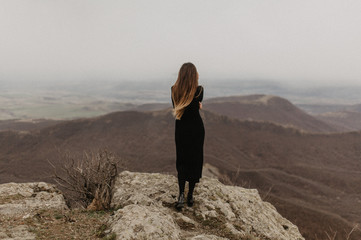 young woman in a black dress standing on the rock