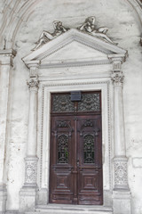 Ancient facade of building with brown door from the street in Vienna, Austria.  Antique door in house with statues located above. Small streets of Vienna with details in architecture. 