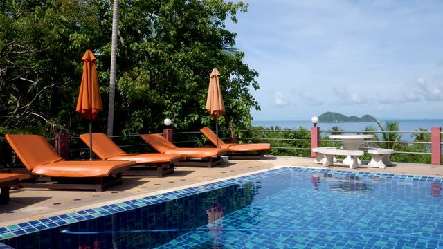 Swimming pool with beach chair and orange umbrellas on sea background in sunlights on home garden. Blue and white tiles background. Vacation or holiday. Clear transparent ripple water background