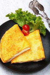 Omelette with cheese on a black porcelain plate. Concept of healthy and delicious breakfasts. Copy of the space.Top view.