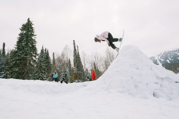 Snowboarder female jumping from kicker in winter sunny day