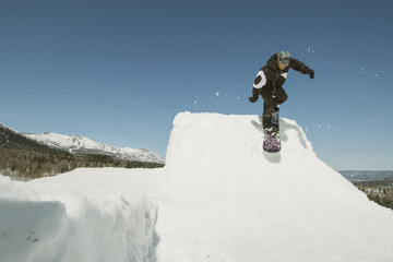 Naklejka na ściany i meble Snowboarder man jumping on quarter pipe snowboard in winter sunny day. Freestyle snowboard training