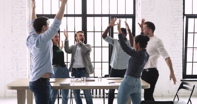 Positive multiracial people joining hands in middle of table, raising team spirit at brainstorming meeting. Overjoyed young diverse colleagues celebrating success, involved in teambuilding activity.