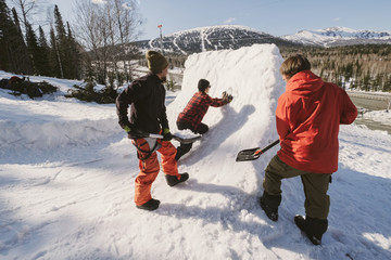 Fototapeta na wymiar Friends snowboarders build quarter pipe snowboard outdoor near ski resort in mountains. Sunny winter day