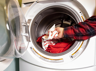 a man in a paid shirt puts colorful laundry in the open door of a front loading electric washing machine