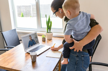 Student mother is watching a lectures, webinars on laptop and writing syllabus with a toddler kid...