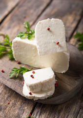 Suluguni cheese is cut into large pieces on a wooden round board. Garnished with parsley leaves,  and pepper.