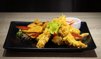 Close-up of delicious crispy fried chicken breast strips with wedges on black plate