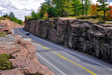 Mountain road cut through the pink granite rock. Landscape with rocks, autumn leaves color, and...