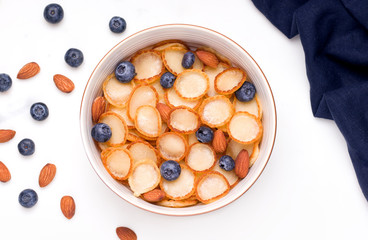Healthy breakfast of tiny pancake cereal with blueberries and nuts on a white plate. View from above