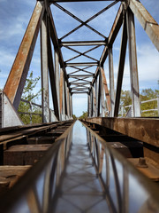 A rusted railroad bridge on a sunny day with cloudy blue sky on the background.