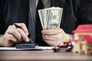 Business man counting money dollar note calculating home and car loans - personal financial insurance lifestyle real estate concept