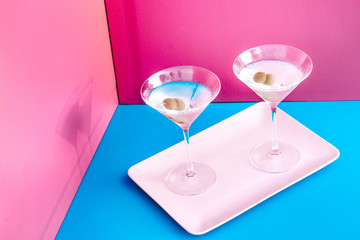 Close up of dry martini with green olive served cold on blue and pink background