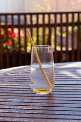 glass of water with straw on wooden garden table, summer soda