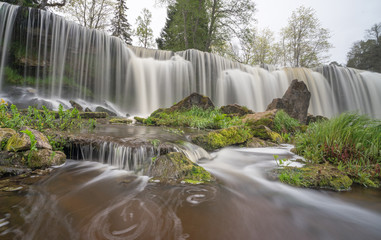 Waterfall in the lower course of the Keila River on North Estonian Klint.  Keila-Joa Castle Schloss Fall (Keila Joa . Smooth surface, broken and fallen rocks and grass, cloudy skyscape. Estonia.