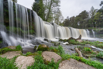 Waterfall in the lower course of the Keila River on North Estonian Klint.  Keila-Joa Castle Schloss Fall (Keila Joa . Smooth surface, broken and fallen rocks and grass, cloudy skyscape. Estonia.