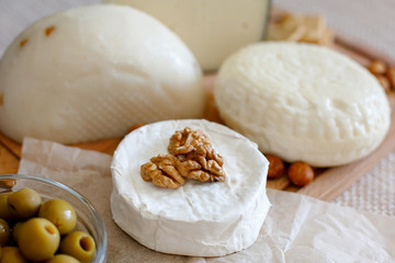 Cheese mix on a wooden plate decorated with grapes, nuts, salad and olives with cheese knifes 