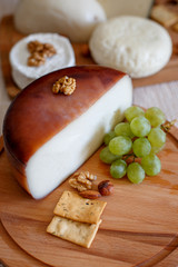 Cheese mix on a wooden plate decorated with grapes, nuts, salad and olives with cheese knifes 